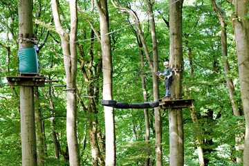 Two children in forest adventure park. Kids boys in helmet climbs on high rope trail. Agility skills and climbing outdoor amusement center for children. Outdoors activity for kid and families.