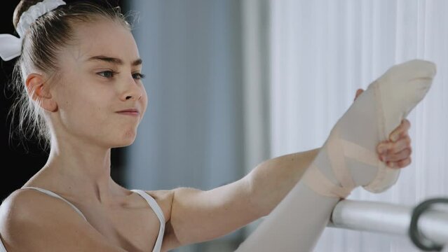 Portrait strong flexible professional teen ballerina caucasian child kid teenager girl dancer doing stretch choreographic exercise at dance school class near ballet barre stretching leg bending knee
