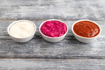 ceramic sauce bowls with horseradish, tomato sauce and mayonnaise on a gray. Side view, copy space.