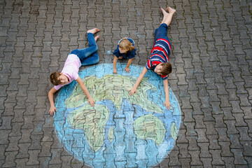 Little preschool girl and two school kids boys with earth globe painting with colorful chalks on...