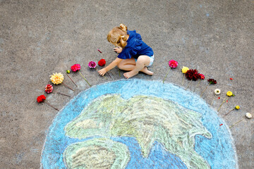 Little preschool girl with flowers and earth globe painting with colorful chalks on ground. Positive toddler child. Happy peace day concept. Creation of children for saving world, environment