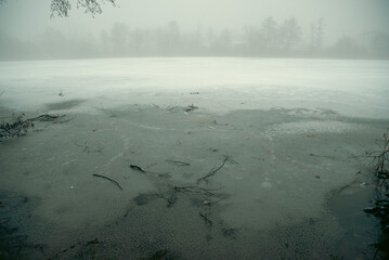 frozen lake with a forest in the background, poor visibility through the fog
