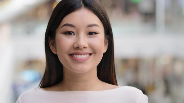 Asian headshot happy optimistic millennial girl 20s brunette woman with natural make-up businesswoman wife girlfriend teacher worker turns head looking at camera smiling friendly carefree female face