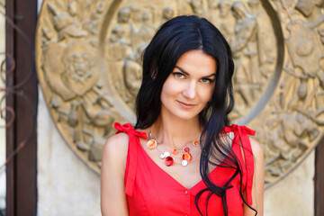 A beautiful young woman with long black hair poses against the background of the city in a red dress