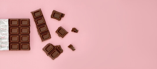 natural bitter chocolate broken pieces on pink background banner, top view, copy space