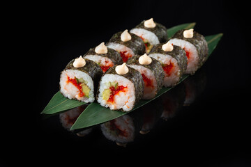Traditional delicious fresh sushi roll set on a black background with reflection. Sushi roll with rice, nori, cream cheese, tobiko caviar, avocado. Sushi menu. Japanese kitchen. Asian food