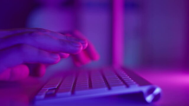 Male hands are typing on the keyboard, typing text and press enter. Slow motion footage with smooth motion. Neon light. High quality 4k footage