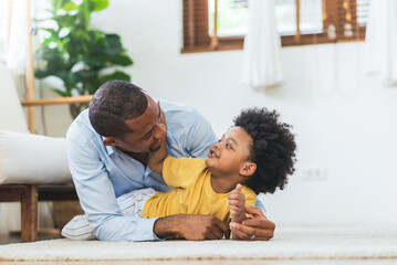 Happy African American Father and little child son playing on the floor at home together, Black...