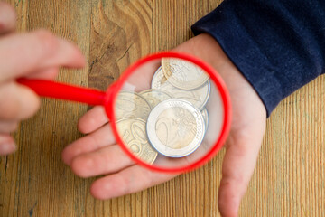 Euro coins magnified by hand magnifier. The young man holds a magnifying glass over the coins. The concept of inflation, poverty, economic crisis.