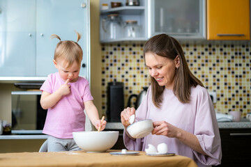 Little cute funny girl helping mother prepare pie cake in kitchen, baking homemade cookie together, happy family time