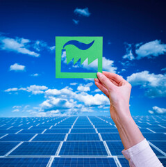 Hand holds green idustry symbol on solar panels background.