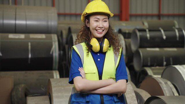 Portrait Asian woman worker industry wears a uniform, helmet, soundproof cover, standing, arms crossed, smiling in the factory.