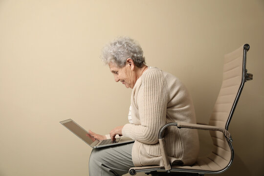 Elderly Woman With Poor Posture Using Laptop On Beige Background