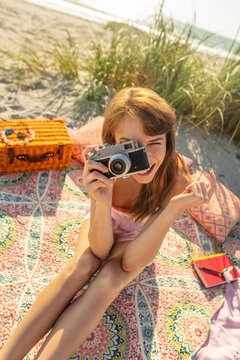 Young Caucasian girl sitting taking photo on beach