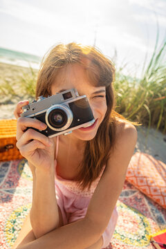 Smiling Caucasian girl with camera photographing beach vacation