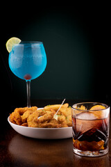 gourmet happyhour - fish and chips, negroni and blue curacao on wooden table.