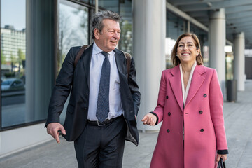 Confident business partners walking down the city and talking about work, handsome senior man with attractive mature woman leader of law office going to the office