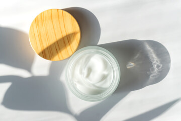 Moisturizer cream jar in frosted glass bottle and leaves shadow on white background. Flat lay, top view. Set for skin and body care beauty products