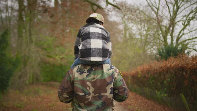 Rear view of American soldier in uniform returning home to family on leave carrying son wearing army cap on shoulders - shot in slow motion
