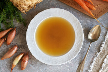 Homemade bone broth in a soup plate with carrots, onions and celery root