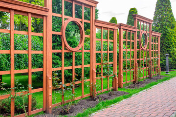 Fototapeta na wymiar Vertical pergola made of wood in a rose garden with a stone tile walkway and ground lantern in the backyard in a garden with plants and a green lawn on a spring day, nobody.