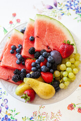 Sliced fruits and berries on a beautiful white plate. Watermelon, strawberry, blueberries, blackberry and grapes. Dietary fruit salad for breakfast, weight loss concept. Healthy snack.