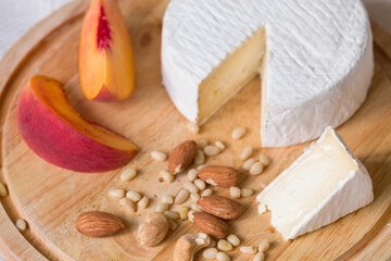 Camembert Cheese on a wooden board with almonds, cashews, pine nuts and peach. French home soft cheese. Selective focus on nuts
