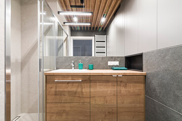 Łazienka z umywalką, baterią, dużym lustrem oraz kabiną prysznicową. Toaleta w mieszkaniu. Kolory szarości i drewno
