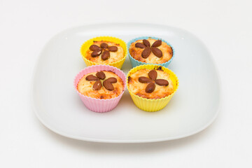 Close-up of homemade vanilla cakes with whole almonds in multicolored silicone cups on a white plate. Healthy snack.