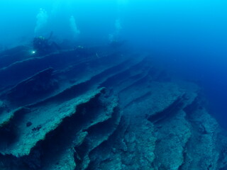Fototapeta na wymiar scuba divers around a reef underwater deep blue water big rock 