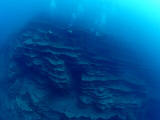 scuba divers around a reef underwater deep blue water big rock 