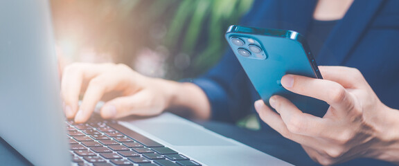 Woman working with a laptop computer and uses a cell phone in the office.