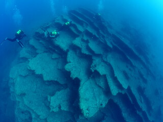 scuba divers around a reef underwater deep blue water big rock 