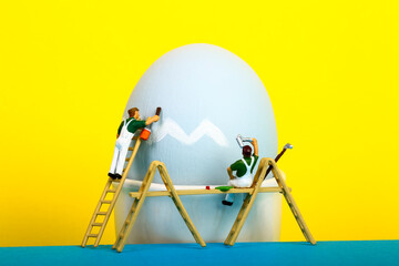 Conceptual image of miniature figure people painting a hens egg for Easter