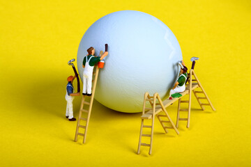 Conceptual image of miniature figure people painting a hens egg for Easter