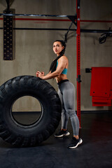 Fototapeta na wymiar Fit female athlete working out with a huge tire, turning and flipping in the gym. Crossfit woman exercising with big tire.