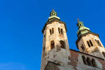 Fototapeta na wymiar Two gothic towers in old Krakow at sunset in the rays of the evening sun against the blue sky