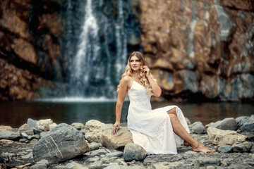 beautiful young woman in a white dress in the mountains near the river on the background of a waterfall