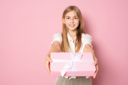 Picture of happy little girl standing isolated over pink background. Looking camera holding gift box surprise.