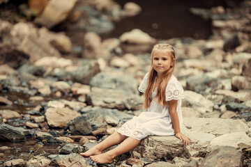 beautiful little girl in a white dress in the mountains near the river on the background of a waterfall