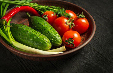 Set of fresh vegetables for salad. Red tomatoes and green young onions with cucumber on a vintage brown plate. Vitamin breakfast or dinner