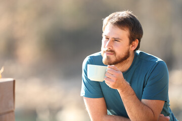 Man contemplating holding a coffee mug in nature