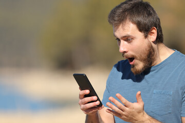 Shocked man checking smart phone in nature