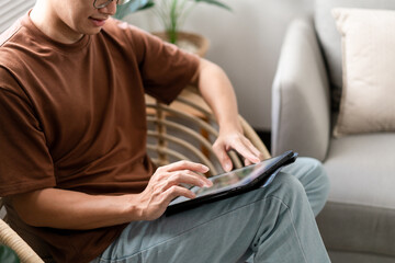 Technology Concept The male with his casual T-shirt and jeans sitting comfortably on the wooden chair and doing touchscreen for checking the web browser on the iPad