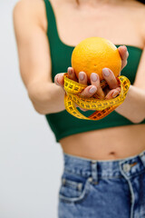 Cellulite is consequence of poor nutrition. Nutritionist holding measuring tape with orange fruit,...