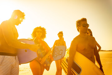 Beach resort at sunset with friends carrying bodyboards