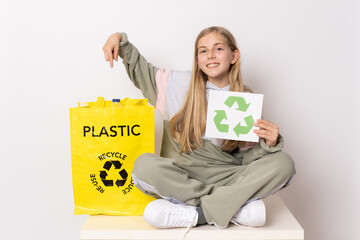 Adorable caucasian girl holding recycling sign pointing plastic recycling bag isolated over white background. Recycling concept.