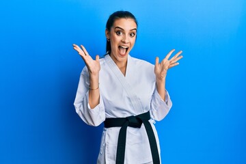 Beautiful brunette young woman wearing karate fighter uniform with black belt celebrating crazy and amazed for success with arms raised and open eyes screaming excited. winner concept © Krakenimages.com