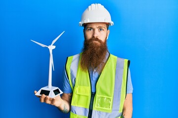 Redhead man with long beard holding solar windmill for renewable electricity thinking attitude and sober expression looking self confident