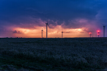 Photograph of large wind turbines in a row in the meadow during a lightning storm
